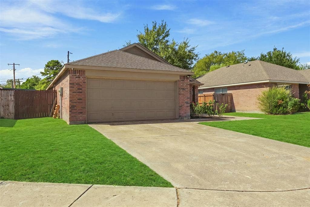 Brick exterior, attached garage, concrete driveway, wood privacy fence, and established landscaping