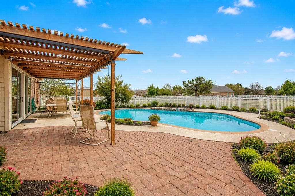1908 Meadow Springs Drive, Haslet, TX 76052 Expansive brick paver patio with a wooden pergola, leading to a curved swimming pool