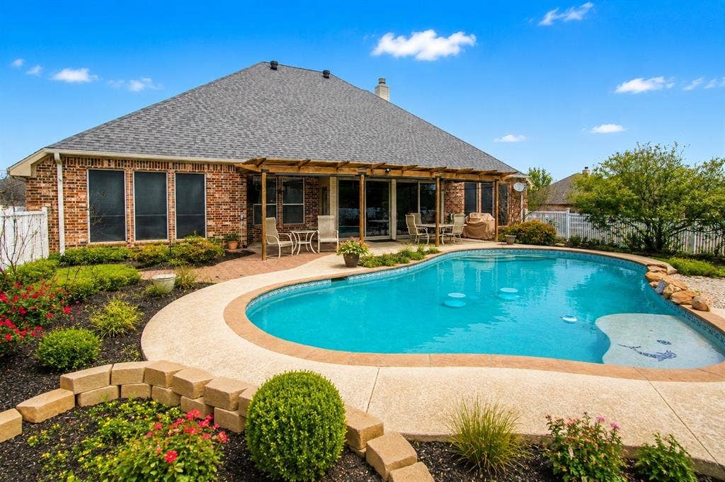 1908 Meadow Springs Drive, Haslet, TX 76052 Brick exterior with multiple windows, covered patio, a shaped pool with integrated steps, and landscaped garden beds
