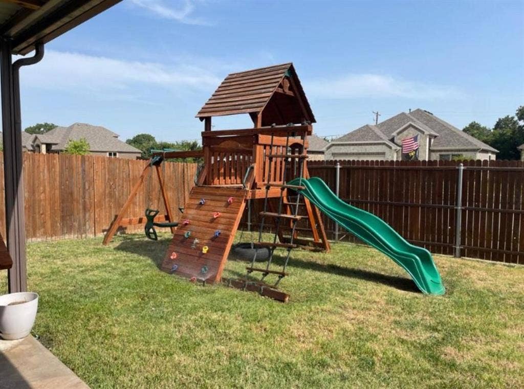 632 Redwood Drive, Greenville, TX 75402 Expansive backyard featuring a wood privacy fence, green lawn, and a multi-level playset with a slide and climbing wall