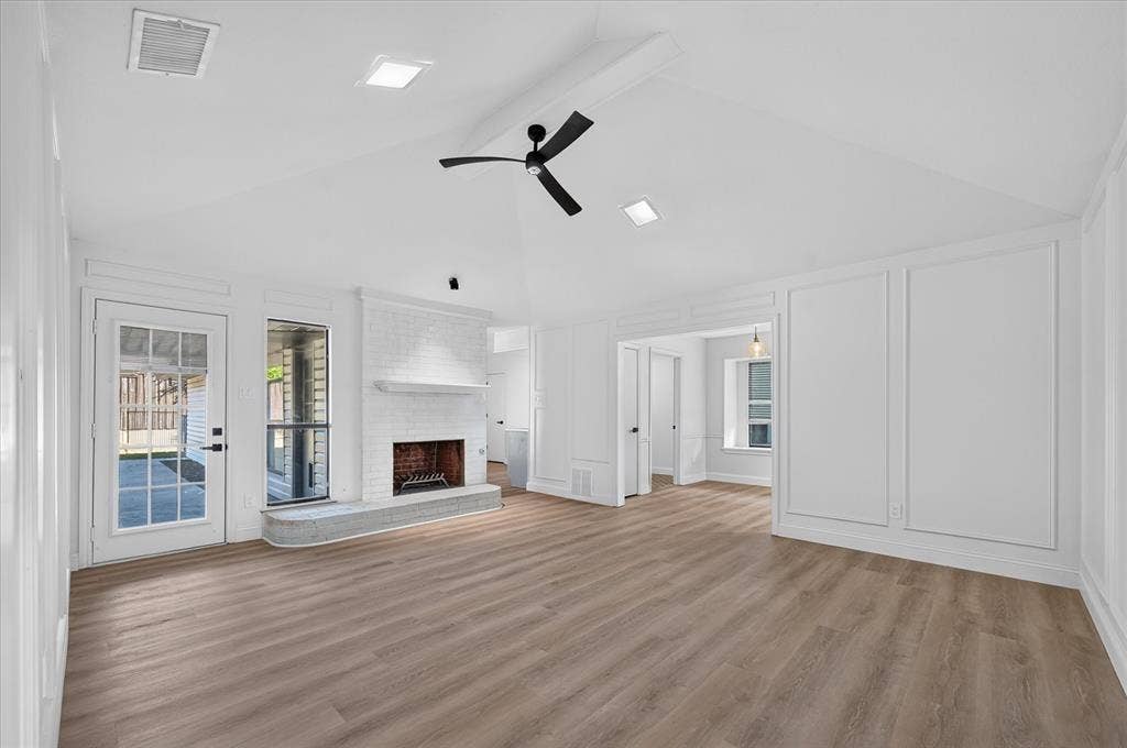 1528 Estrella Drive, Plano, TX 75074 Vaulted ceiling with a ceiling fan, brick fireplace with a stone hearth, wood-finish flooring, accent wall paneling, and a full-light glass door