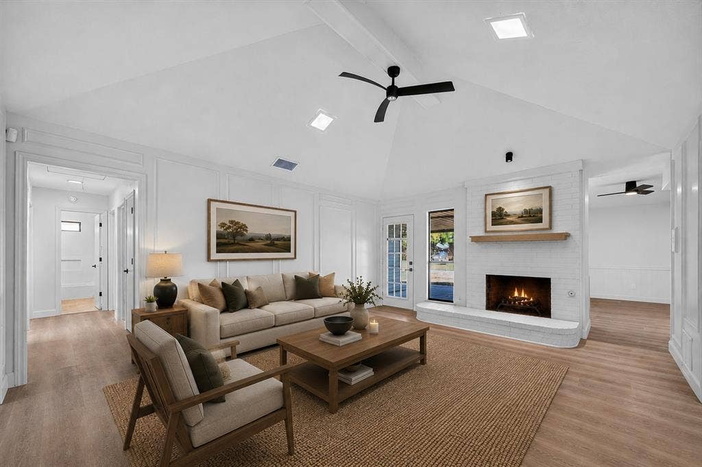 1528 Estrella Drive, Plano, TX 75074 Vaulted white ceiling with exposed beam, white painted brick fireplace, wood-finish flooring, white paneling, and a ceiling fan