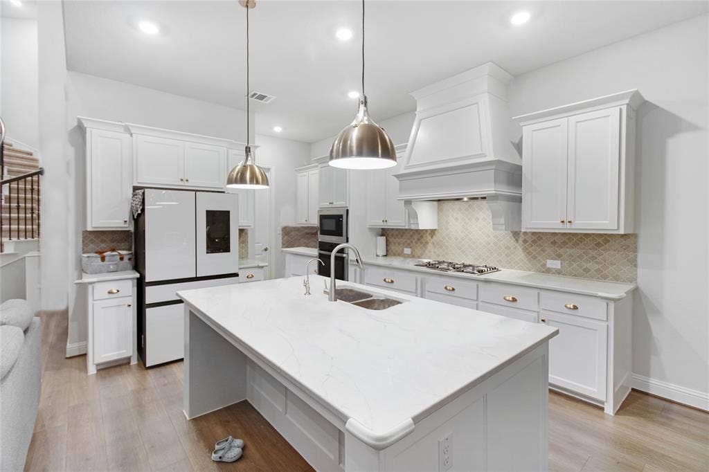 1531 20th street, Argyle, TX 76226 White cabinetry with gold-tone hardware, wood-finish flooring, recessed lighting, and a kitchen island with a double basin sink