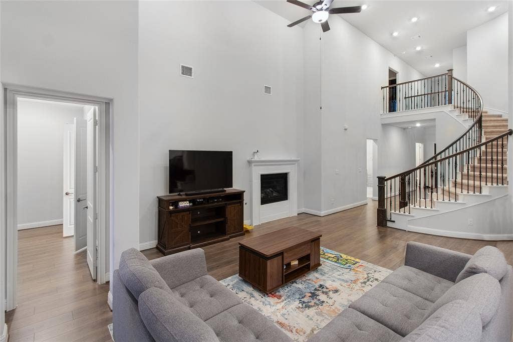 1531 20th street, Argyle, TX 76226 Spacious open-concept living area featuring soaring ceilings with recessed lighting and a ceiling fan, hardwood flooring throughout, and a curved staircase with black metal railings