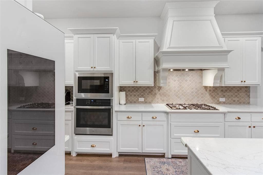 1531 20th street, Argyle, TX 76226 White cabinetry with brass hardware, stainless steel built-in appliances, a gas cooktop, patterned tile backsplash, and light-toned countertops