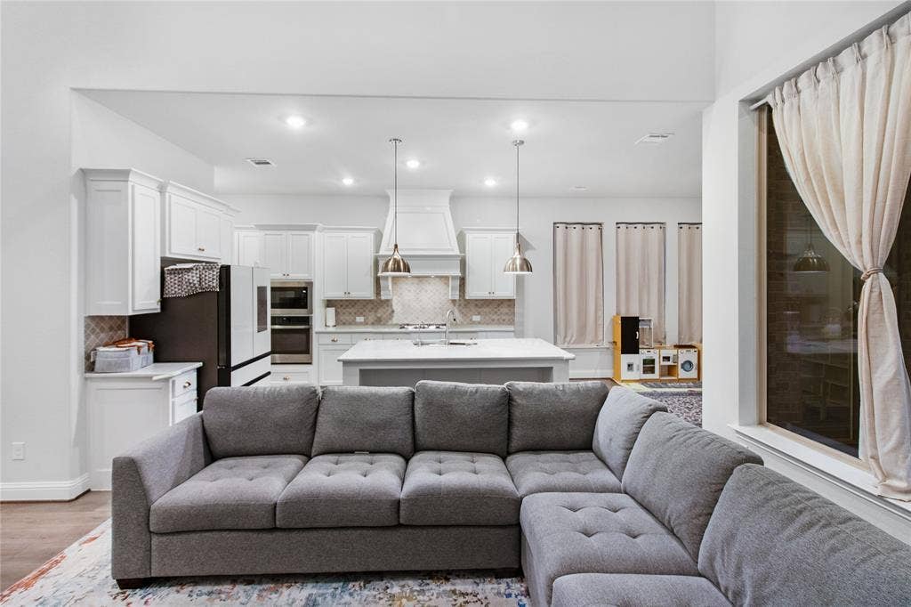1531 20th street, Argyle, TX 76226 Open-concept living and kitchen featuring a gray upholstered sectional sofa, pendant lighting above the kitchen island, stainless steel appliances, white cabinetry, and recessed ceiling lights throughout the space