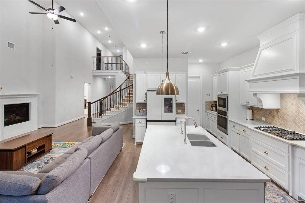 1531 20th street, Argyle, TX 76226 Open-concept living and dining space featuring a white kitchen with gas cooktop, stainless steel appliances, white cabinetry, and a quartz waterfall island
