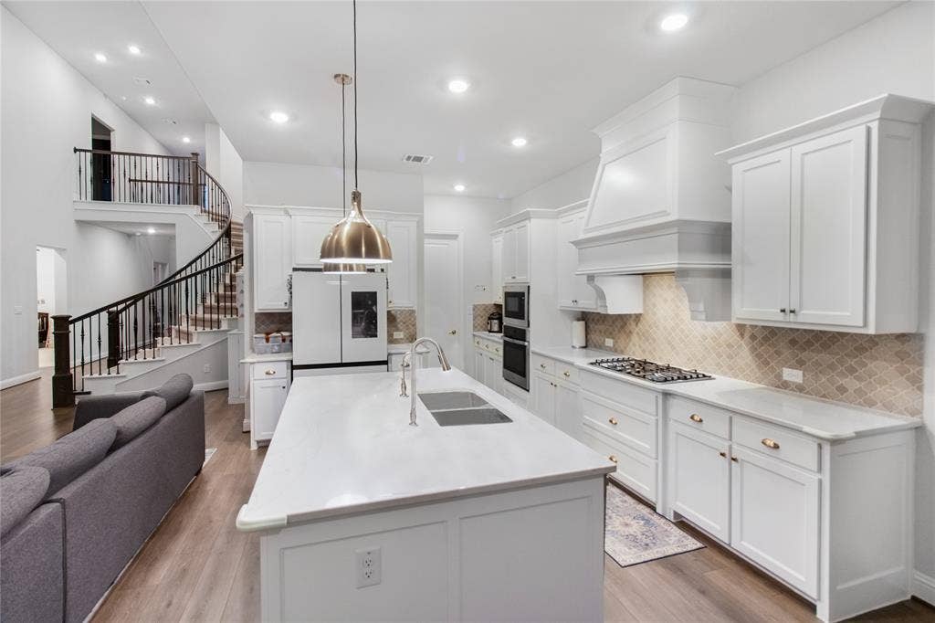 1531 20th street, Argyle, TX 76226 Contemporary kitchen featuring white cabinetry, a large center island with white quartz countertop, stainless steel appliances including a gas cooktop and built-in refrigerator, pendant lighting, and subway tile backsplash