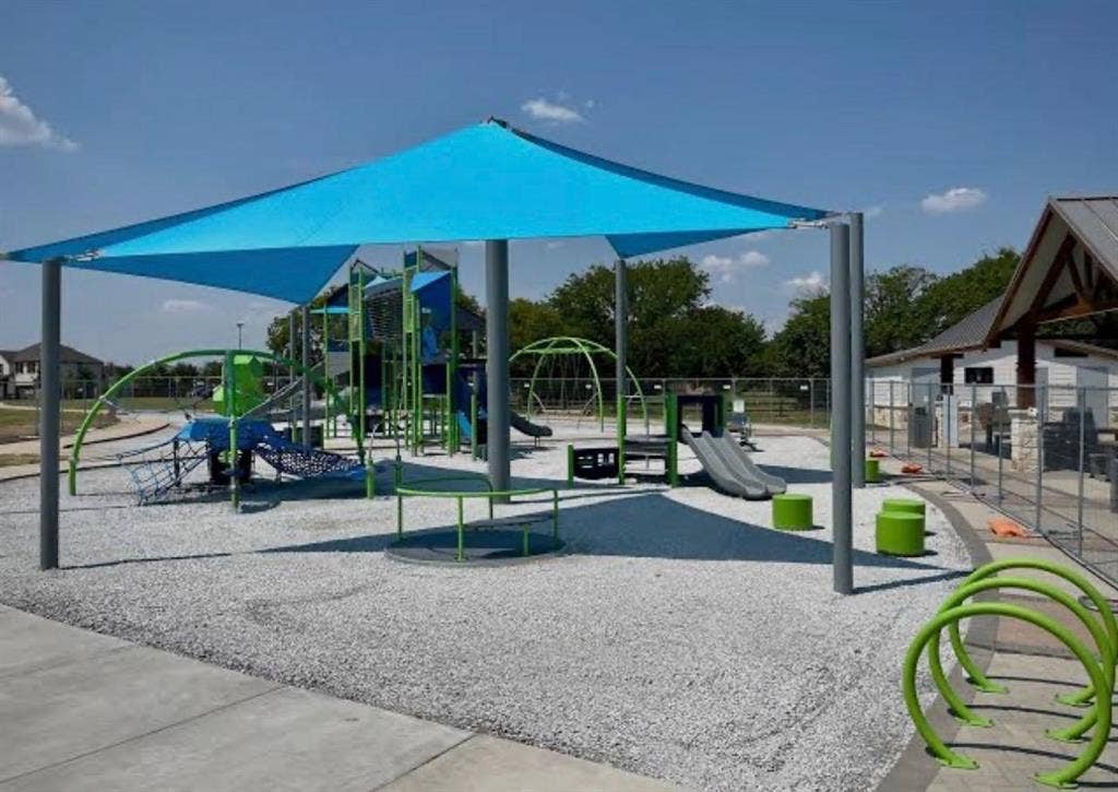 7204 Running Iron Trail, Sachse, TX 75048 Playground featuring a blue shade structure, multiple play elements, a rubberized safety surface, and a nearby covered pavilion