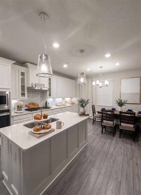 7204 Running Iron Trail, Sachse, TX 75048 Kitchen with a large island featuring an undermount sink and light-toned countertop, white cabinetry, stainless steel appliances, and a tile backsplash