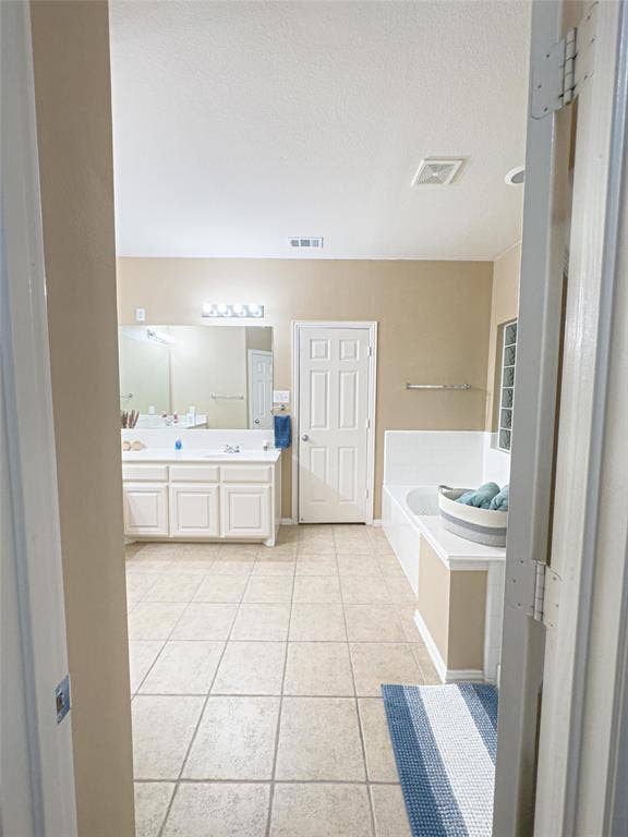 12146 Gonzales Drive, Frisco, TX 75035 Bathroom featuring tile patterned floors, a garden tub, double vanity, and a textured ceiling