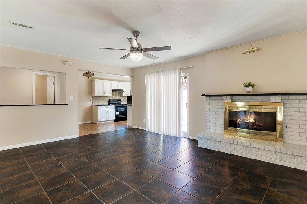 925 Lombardy Drive, Plano, TX 75023 Tile flooring, white brick fireplace with brass trim, sliding glass door, ceiling fan with integrated lighting, and kitchen pass-through window