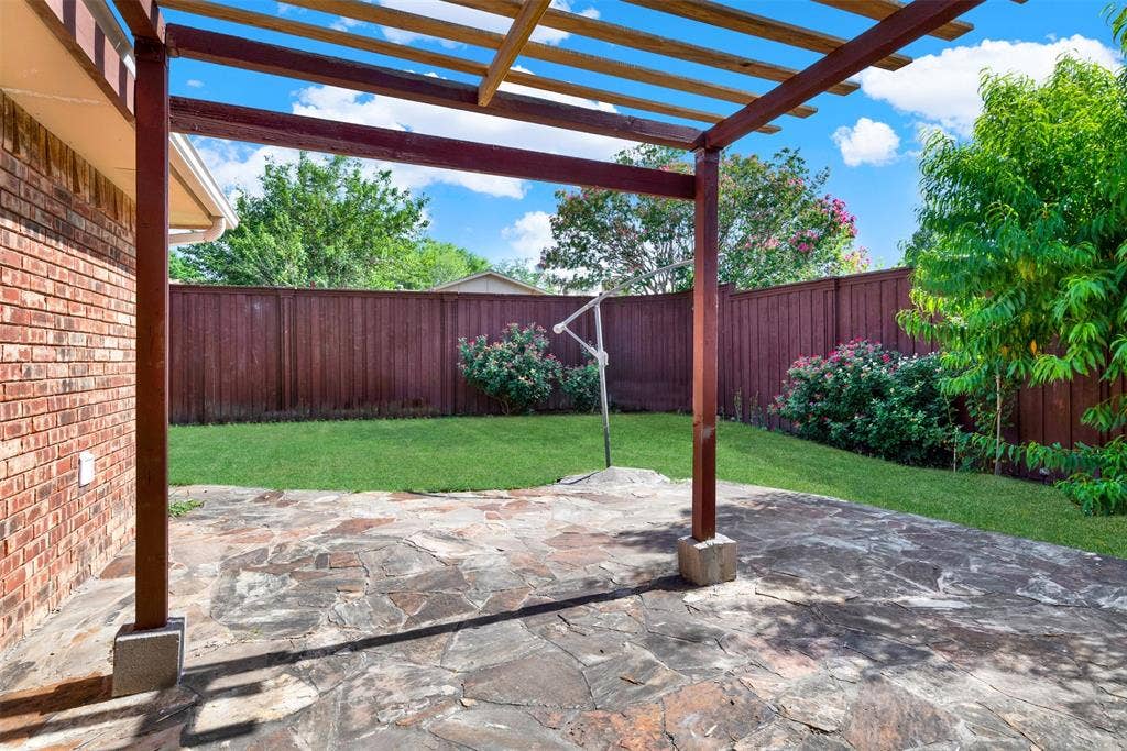 925 Lombardy Drive, Plano, TX 75023 Expansive stone patio with overhead pergola, brick exterior, fenced yard, and established landscaping