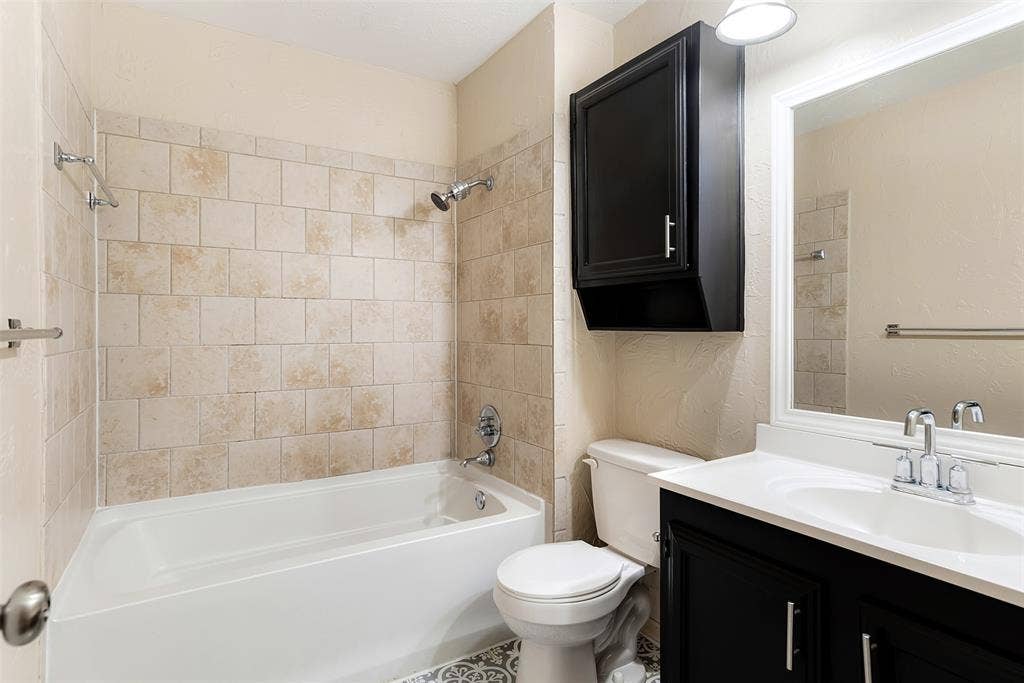 925 Lombardy Drive, Plano, TX 75023 Bathroom featuring a white bathtub, ceramic tile shower surround, dark wood-finish vanity with an integrated sink, wall-mounted mirror, and patterned floor tile