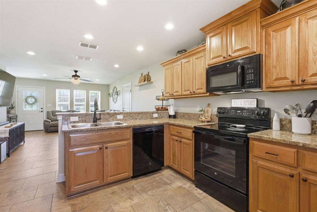 213 Freeman Street, Lindale, TX 75771 Kitchen featuring wood-finish cabinetry, granite countertops, an undermount double basin sink, and black appliances