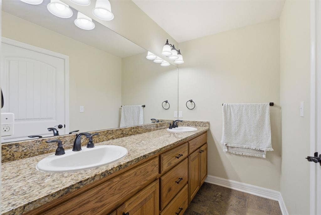 213 Freeman Street, Lindale, TX 75771 Dual vanity with a stone-finish countertop, wood-finish cabinetry, and oil-rubbed bronze fixtures