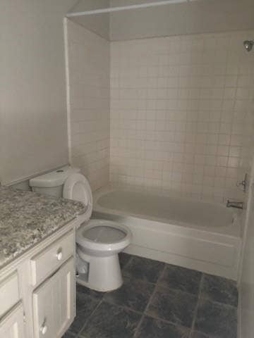 2805 Woodmont Trail, Fort Worth, TX 76133 White tile surround bathtub with shower fixture, dark tile flooring, white vanity with a speckled countertop, and a white toilet