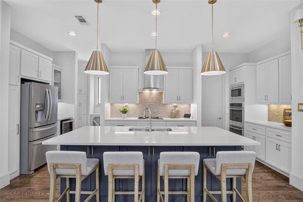 5328 Manett Street, Dallas, TX 75206 Gourmet kitchen featuring a large central island, white cabinetry, stainless steel appliances, and wood-finish flooring
