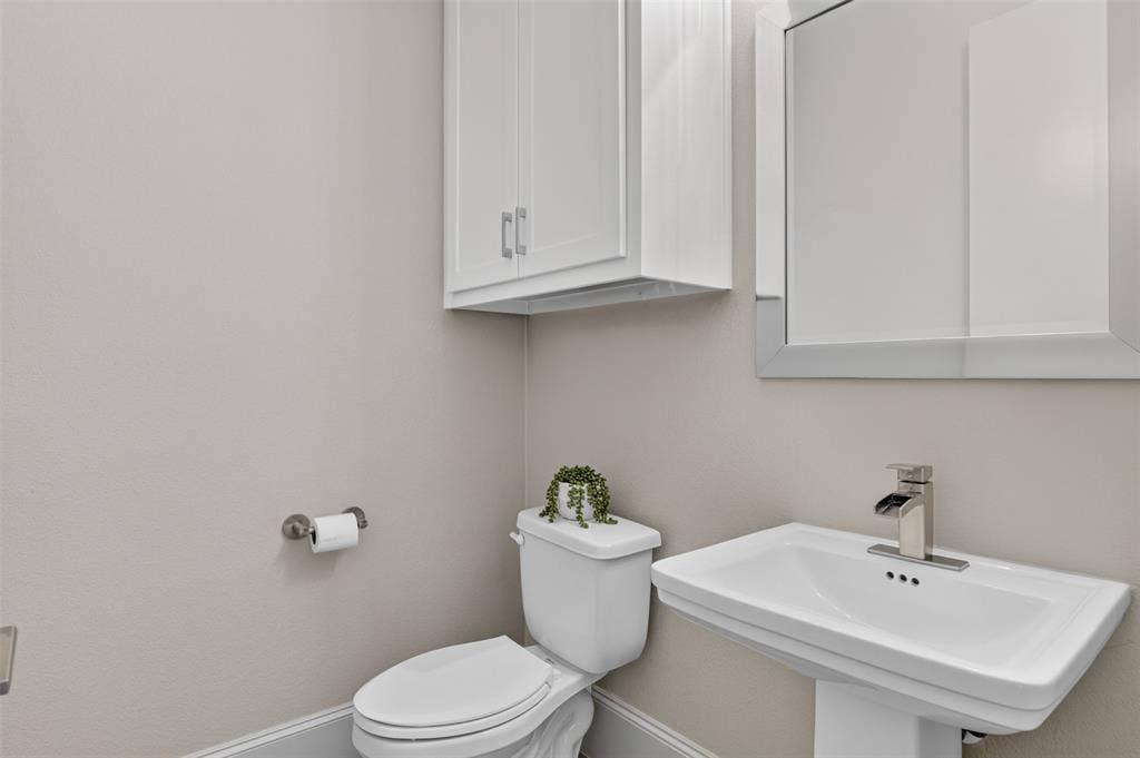 5328 Manett Street, Dallas, TX 75206 Pedestal sink with a polished chrome faucet, framed mirror, and wall-mounted storage cabinet