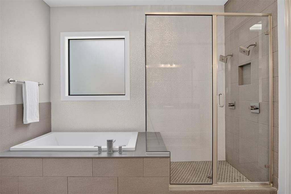 5328 Manett Street, Dallas, TX 75206 Built-in soaking tub with deck-mounted fixtures, glass-enclosed shower with tile surround, square window with white trim, and tiled half-wall detailing