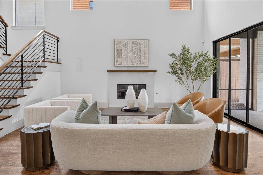 5328 Manett Street, Dallas, TX 75206 Double-height living space featuring a fireplace, wood-finish flooring, a contemporary staircase with iron balusters, and expansive glass doors