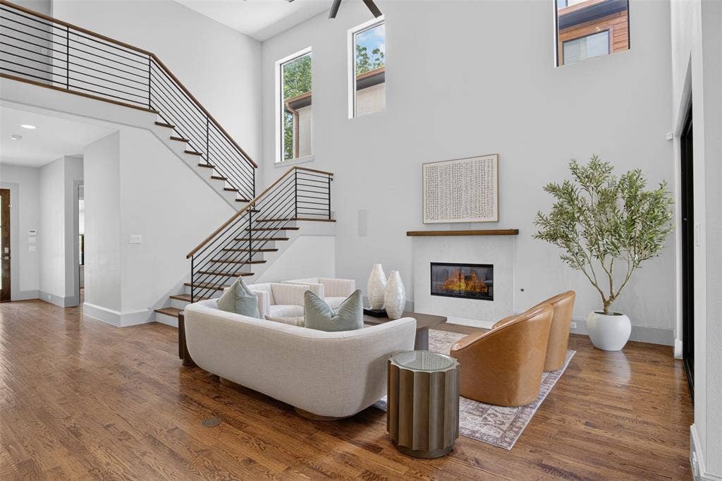 5328 Manett Street, Dallas, TX 75206 Two-story living area with high ceilings, wood-finish flooring, a contemporary fireplace, and a modern staircase featuring horizontal metal railings and wood handrails