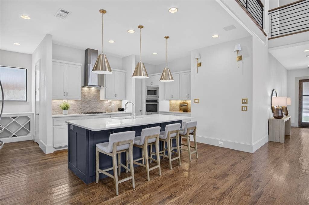 5328 Manett Street, Dallas, TX 75206 Gourmet kitchen with a large center island, built-in wine storage, stainless steel range hood, and wood-finish flooring