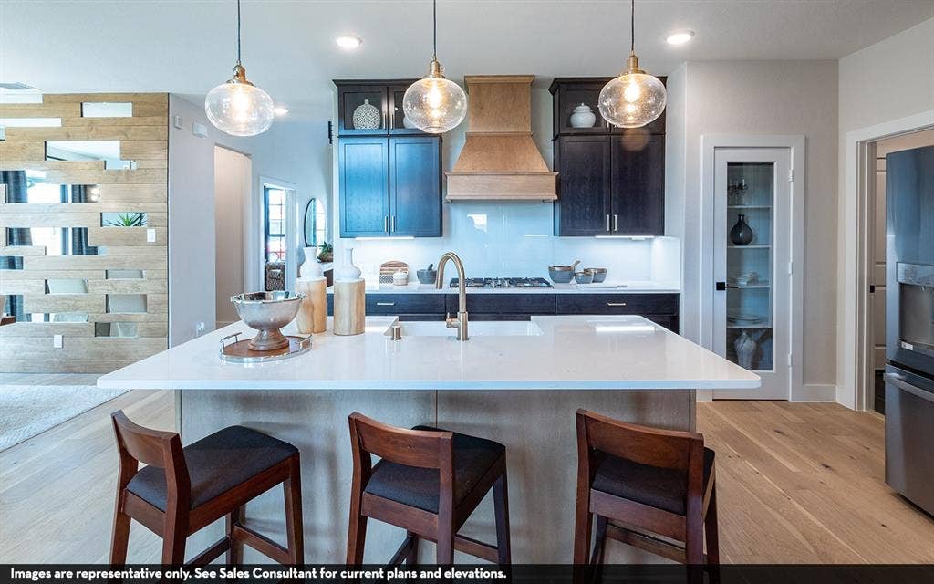 810 Metcalf Drive, Princeton, TX 75071 Kitchen featuring a large island with a light-toned countertop, wood-finish flooring, dark cabinetry, and three pendant light fixtures
