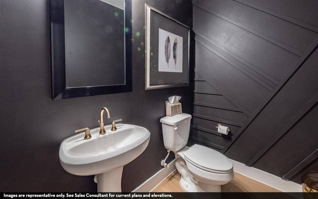 810 Metcalf Drive, Princeton, TX 75071 Pedestal sink with a bronze-finish faucet, dark-framed mirror, and a toilet with a paneled accent wall