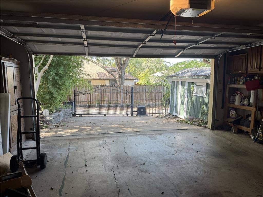 Garage with automatic opener, featuring built-in storage cabinetry, and an exterior wrought iron gate.