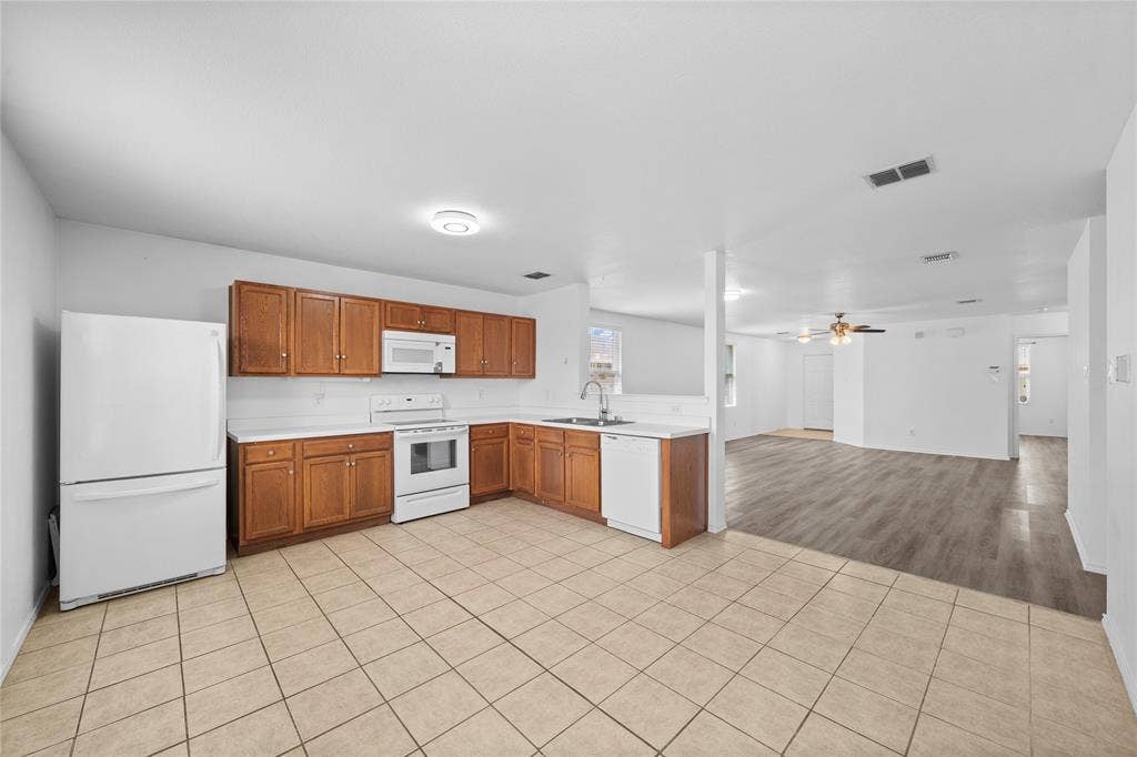 8421 Cotton Valley Lane, Arlington, TX 76002 Kitchen featuring a full suite of white appliances, wood-finish cabinetry, light-toned countertops, and tile flooring