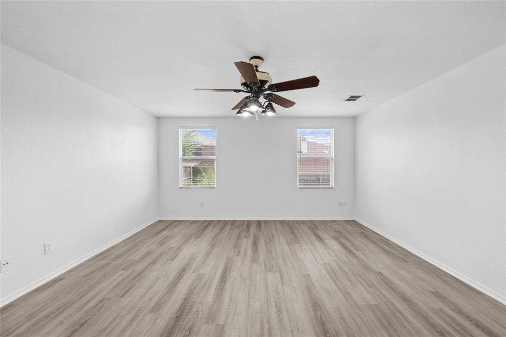 8421 Cotton Valley Lane, Arlington, TX 76002 Spacious room featuring wood-finish flooring, white walls, two windows, and a ceiling fan with integrated lighting