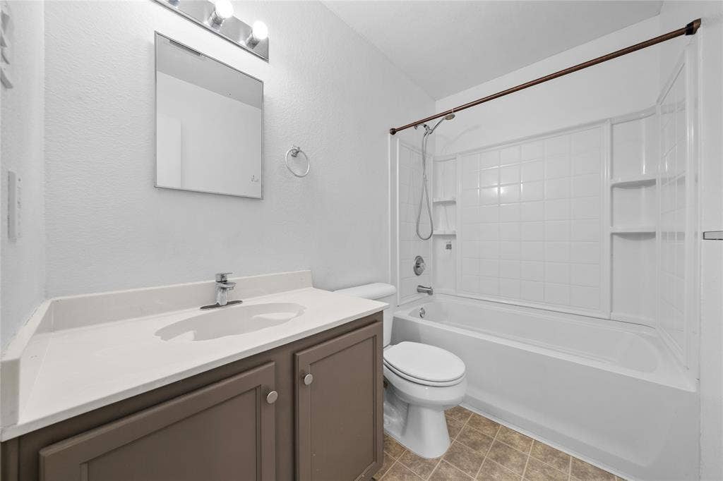 8421 Cotton Valley Lane, Arlington, TX 76002 White tiled shower and bathtub combination with integrated shelving, a rectangular vanity mirror, and a single vanity with storage cabinets