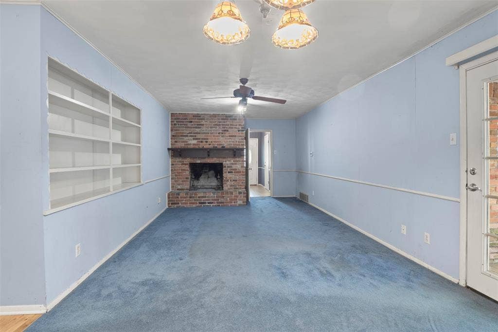 Built-in shelving, brick fireplace with mantel, ceiling fan, and decorative overhead lighting