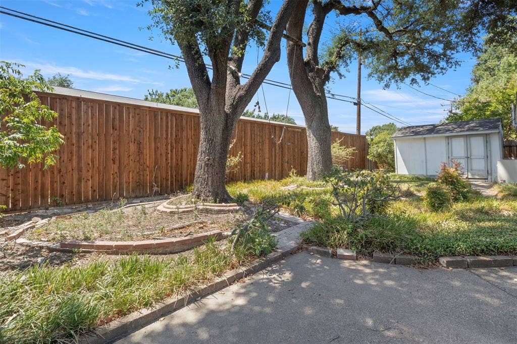 Wood privacy fence, mature trees, brick-lined landscaping, concrete path, and a storage shed