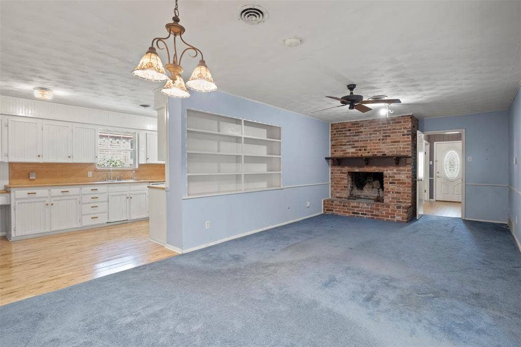 Brick fireplace with a wood mantle, built-in shelving, white cabinetry, wood-finish countertops, and wood-finish flooring
