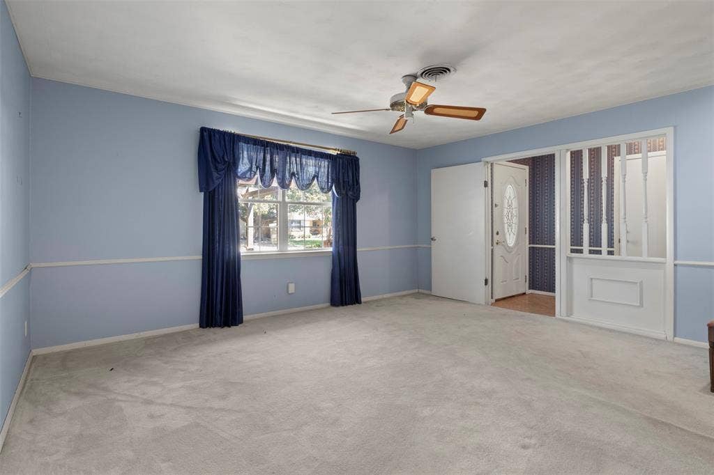 Carpeted room featuring a ceiling fan, a window with exterior views, and a paneled entry door with decorative glass