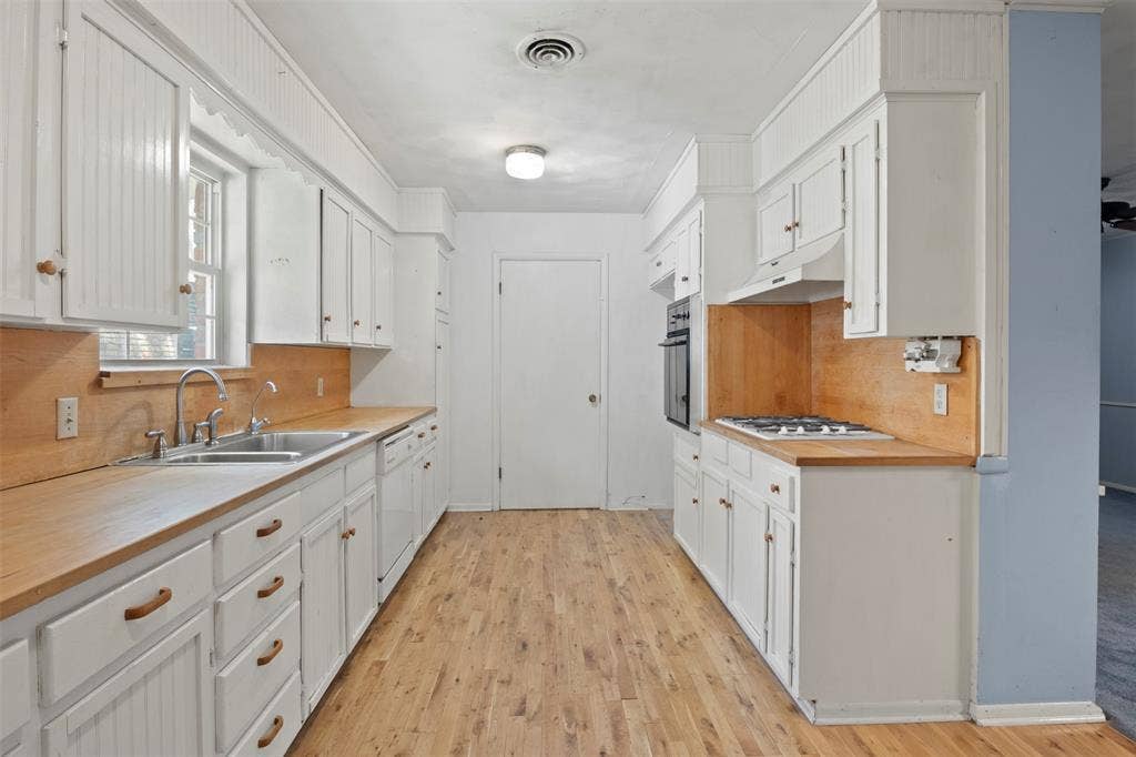 U-shaped kitchen with wood-finish flooring, white cabinetry, integrated dual basin sink, and built-in oven with gas cooktop