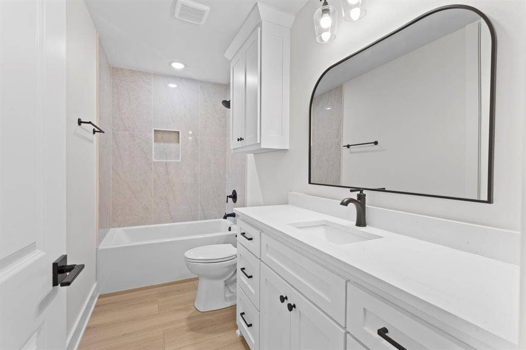 13914 Cedar Hill Lane, Tyler, TX 75704 White vanity with integrated sink and matte black faucet, arched framed mirror, white-tiled shower with built-in niche, and wood-finish flooring