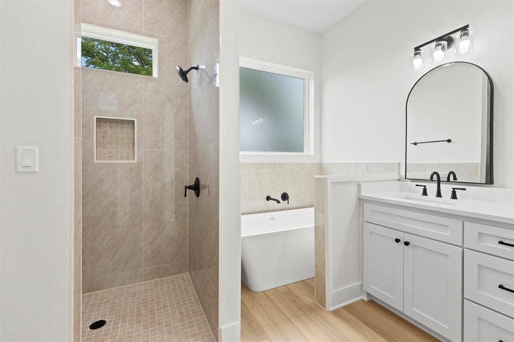13914 Cedar Hill Lane, Tyler, TX 75704 Tiled shower with a niche, freestanding tub, dual-sink vanity with white cabinetry, and wood-finish flooring