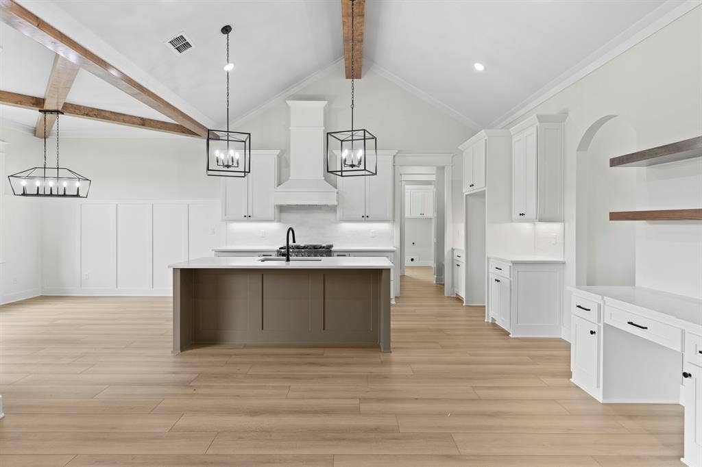 13914 Cedar Hill Lane, Tyler, TX 75704 Vaulted ceiling with exposed wood beams, wood-finish flooring, white cabinetry, kitchen island with integrated sink, and built-in desk area