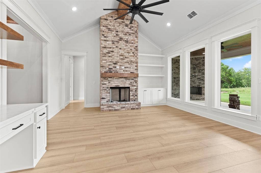 13914 Cedar Hill Lane, Tyler, TX 75704 Vaulted ceiling with exposed beam fan, brick fireplace with wood mantel, built-in shelving and cabinetry, wood-finish flooring, and multiple large windows