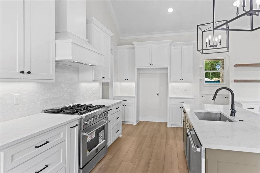 13914 Cedar Hill Lane, Tyler, TX 75704 White shaker cabinetry, stainless steel range, light-toned wood-finish flooring, island with undermount sink, and contemporary chandelier