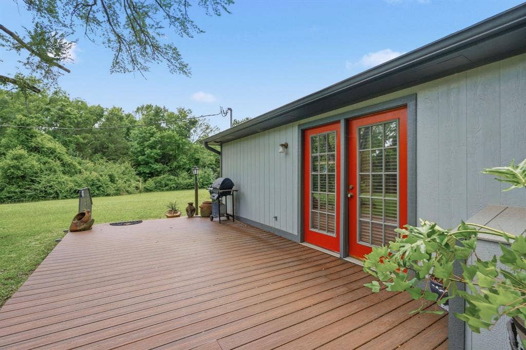 6146 County Road 334, Tyler, TX 75708 Expansive wood-finish deck with vibrant red French doors, light gray siding, and dark gray trim