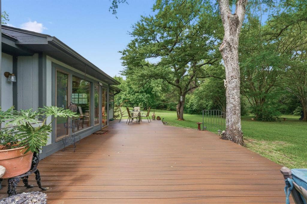 6146 County Road 334, Tyler, TX 75708 Expansive outdoor deck with wood-finish planks, bordered by mature trees and a substantial lawn area