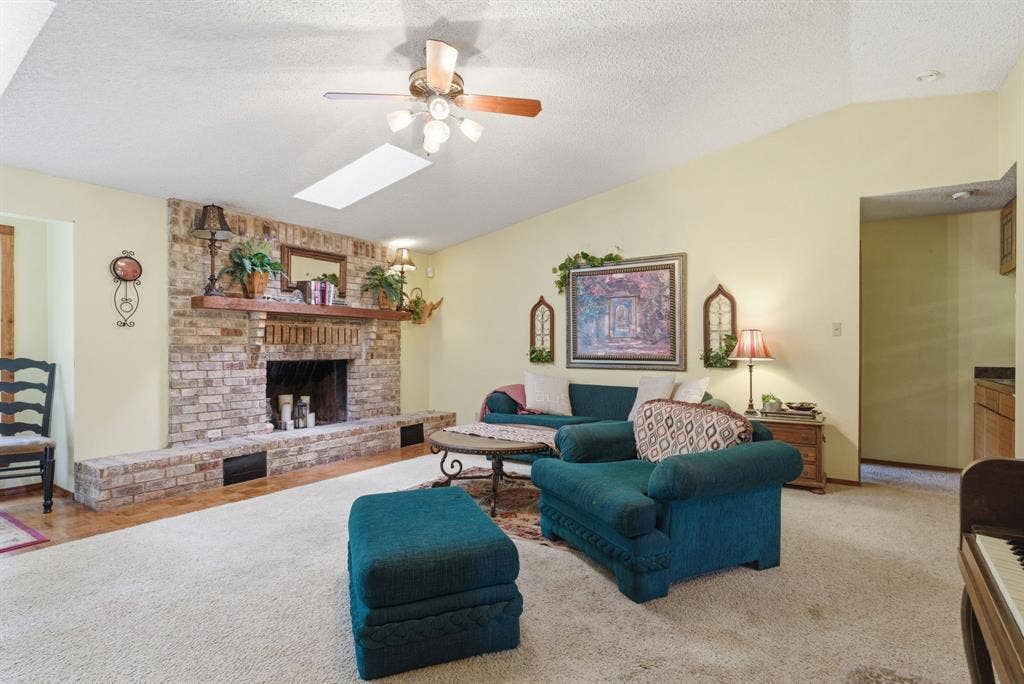 6146 County Road 334, Tyler, TX 75708 Vaulted ceiling with skylight, brick fireplace with wood mantel, ceiling fan with light fixture, and wood-finish flooring
