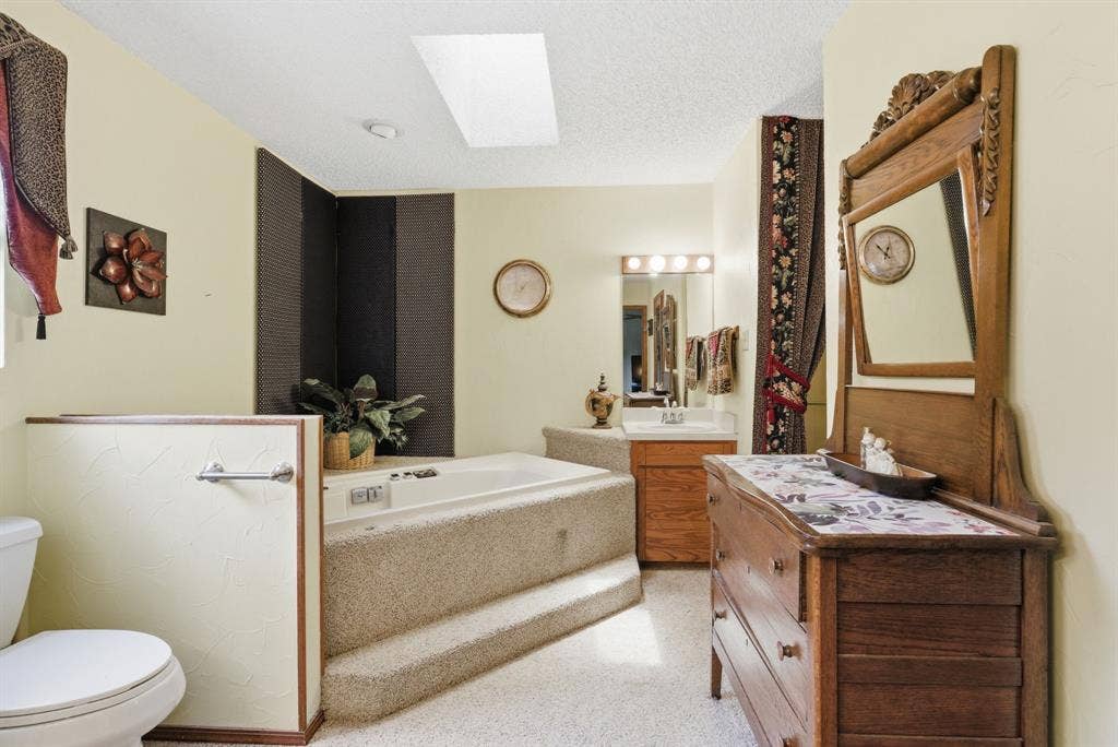 6146 County Road 334, Tyler, TX 75708 Sunken tub with carpeted steps, overhead skylight, and single vanity with a large mirror