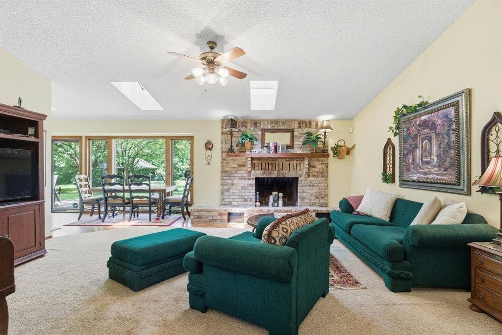 6146 County Road 334, Tyler, TX 75708 Brick fireplace with a wood-finish mantel, skylights, ceiling fan with integrated lighting, and expansive windows