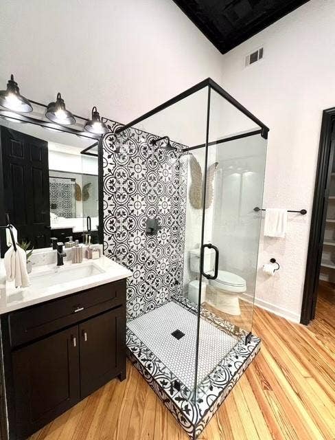 115 E Moore Avenue, #203, Terrell, TX 75160 Walk-in shower with patterned tile surround and hex tile floor, glass enclosure with matte black trim, dark wood-finish vanity with white countertop, wood-finish flooring, and black paneled ceiling