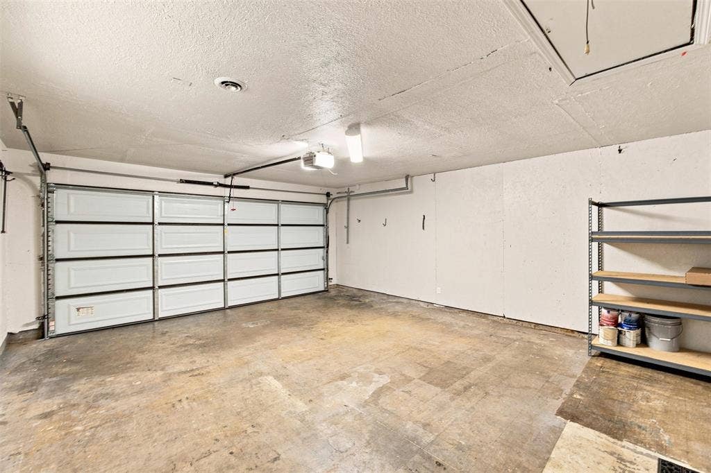 2022 Normandy Drive, Irving, TX 75060 Spacious garage featuring a paneled overhead door, concrete flooring, overhead lighting, and shelving